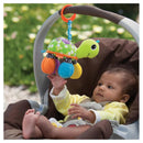 Colorful Infantino Turtle Mirror Pal toy hangs from a stroller as a baby reaches for it, smiling in bright sunlight.