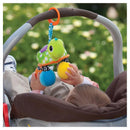 Infantino Turtle Mirror Pal in green, hanging from a stroller, as a baby reaches for colorful plush balls.