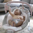 Baby in a soothing bouncer seat reaching for hanging toys, featuring a plush unicorn and flower, with a soft, padded design.
