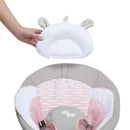 A hand is holding a soft, white unicorn head support for the Ingenuity Soothing Baby Bouncer, showcasing its gentle design.