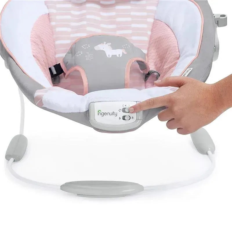 Infant seat bouncer with pink and gray fabric, featuring soothing vibrations; a hand adjusts settings on the control panel.