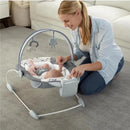 A woman interacts with a baby in the Ingenuity SmartBounce Automatic Baby Bouncer Seat, featuring hanging toys and a soft cushion.