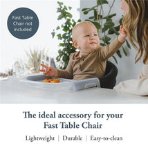 A toddler seated at a table, reaching for food on the Inglesina Fast Dining Tray Plus, with a woman nearby.