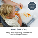 A toddler enjoys messy food on the Inglesina Fast Dining Tray Plus, featuring deep raised edges to minimize spills.