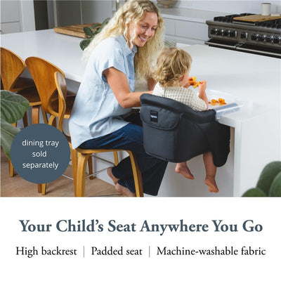 Inglesina Fast Table Chair in black, securely attached to a table, with a child eating. Features a high backrest and padded seat.