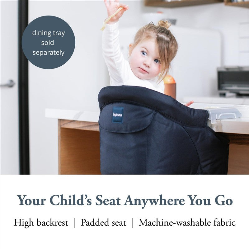 Navy Inglesina Fast Table Chair secured to a dining table with a child excitedly raising their hand; features high backrest and padded seat.