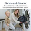 A woman kneels by a washing machine, placing a removable black cover inside while a toddler watches.