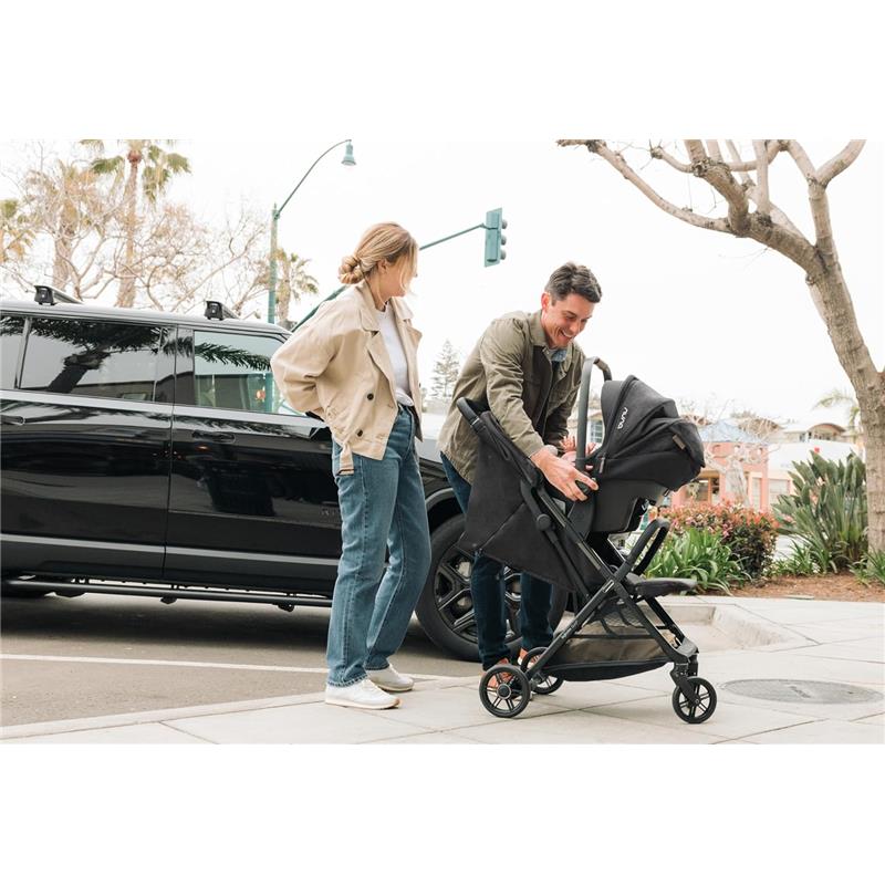 A man is attaching a car seat to the Inglesina Quid³ stroller while a woman observes, next to a black car.