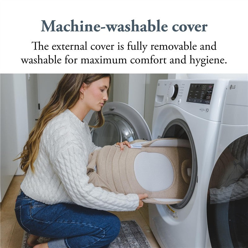 A woman in a white sweater places the Inglesina Welcome Pod Lounger with a beige cover into a washing machine.