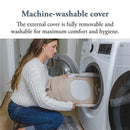 A woman in a white sweater places the Inglesina Welcome Pod Lounger with a beige cover into a washing machine.