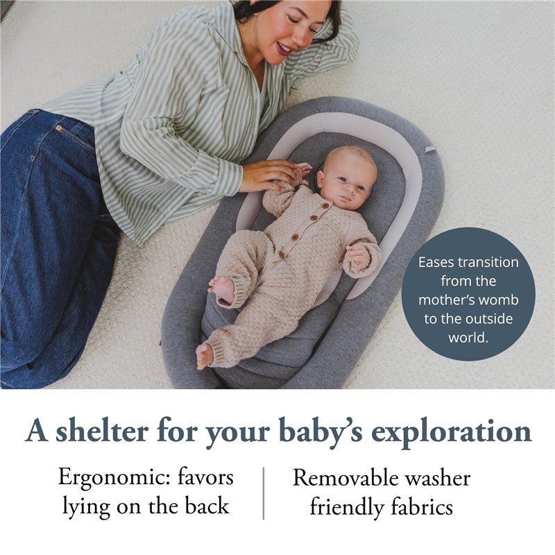 A woman gently interacts with her baby in the Inglesina Welcome Pod Lounger, highlighting its ergonomic design and soft fabric.