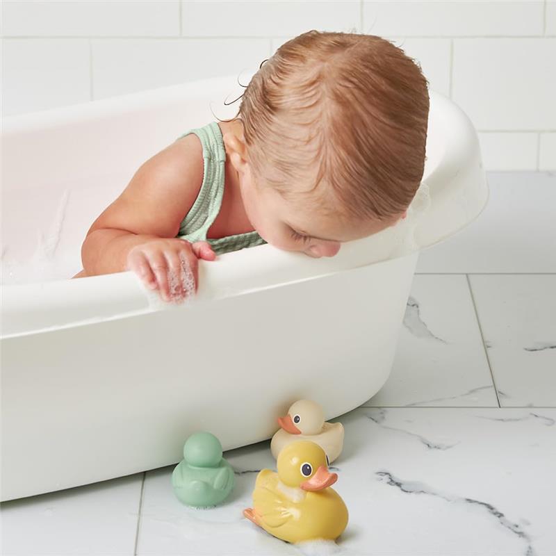 Toddler in a bathtub playing with Itzy Ritzy Ducky Family floating bath toys: green, yellow, and white ducks.