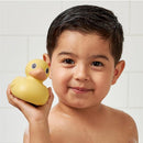 Child smiling while holding a yellow rubber duck toy in a bathroom setting.