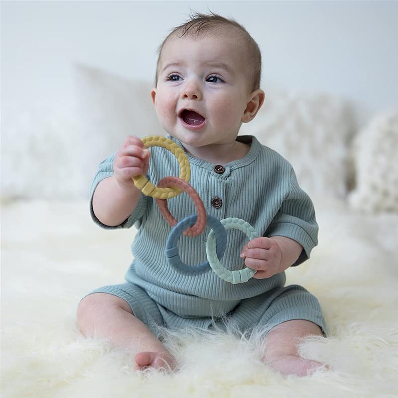 Baby sitting on a soft surface, smiling while holding a set of colorful silicone linking rings in various pastel colors.