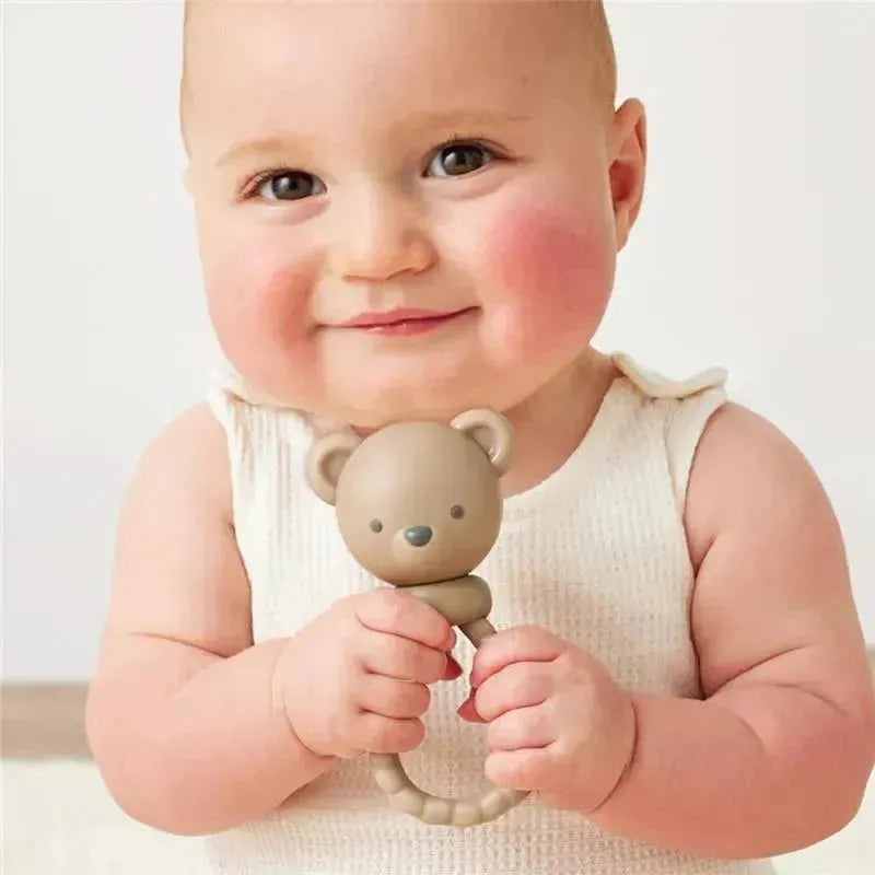 Smiling baby holding a Bear Sweetie Rattle™, a soft toy with a bear head, designed for sensory play.