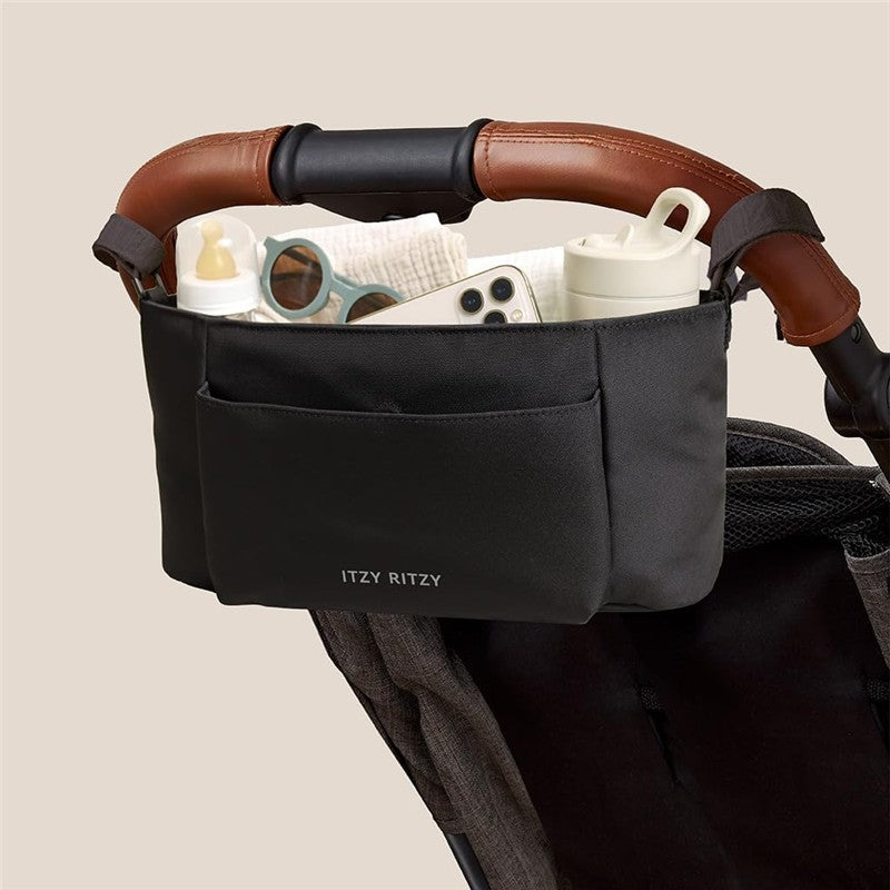 Itzy Ritzy Belong Carry-All Caddy in black, attached to a stroller, holding bottles, sunglasses, and a phone.