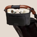 Itzy Ritzy Belong Carry-All Caddy in black, attached to a stroller, holding bottles, sunglasses, and a phone.