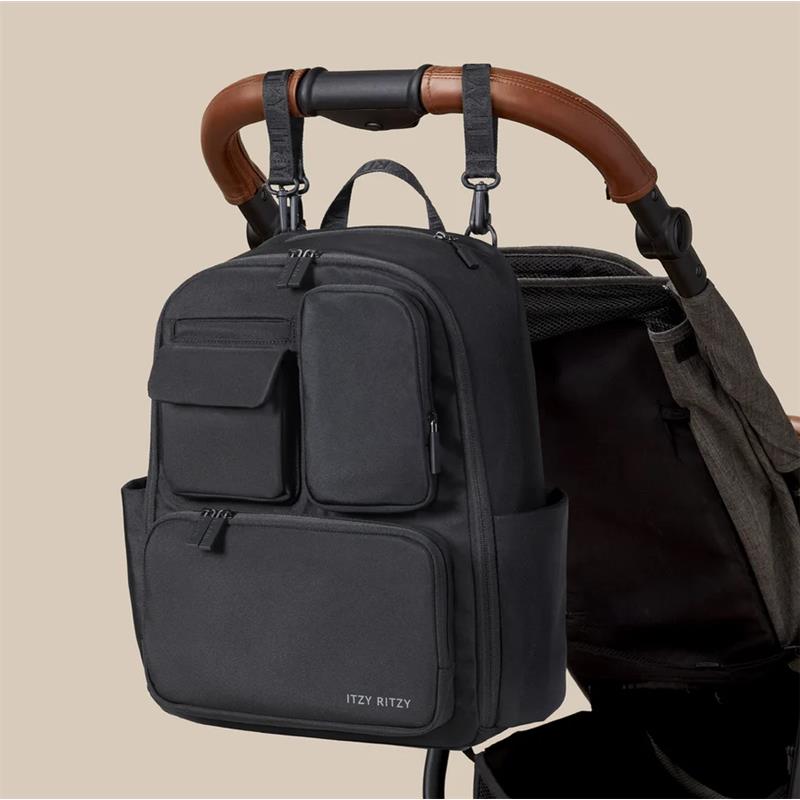 Black Itzy Ritzy Belong Utility Backpack hanging from a stroller handle, featuring multiple zippered pockets and a sleek design.