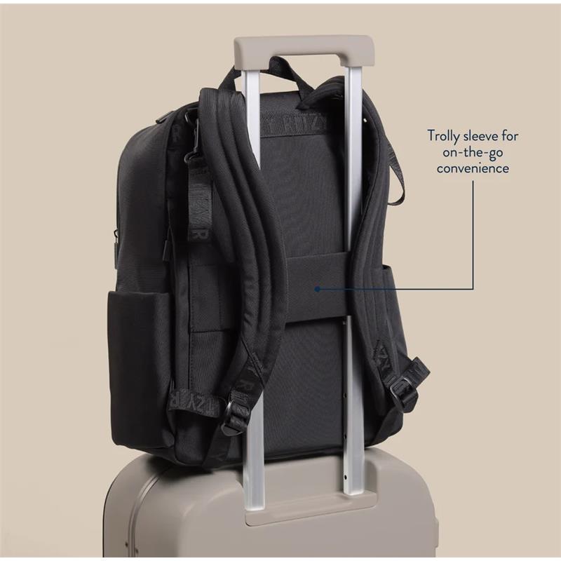Black Itzy Ritzy Belong Utility Backpack with trolley sleeve, displayed on top of a suitcase for travel convenience.