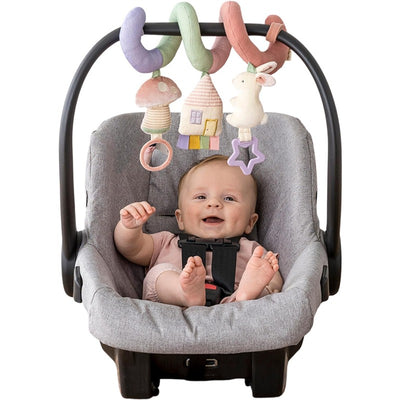 Infant in a car seat smiles, playing with colorful hanging toys including a mushroom, house, and bunny.