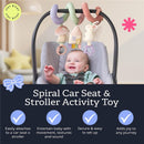 Pastel spiral activity toy featuring a mushroom, house, and bunny, attached to a car seat. Smiling baby interacts with it.