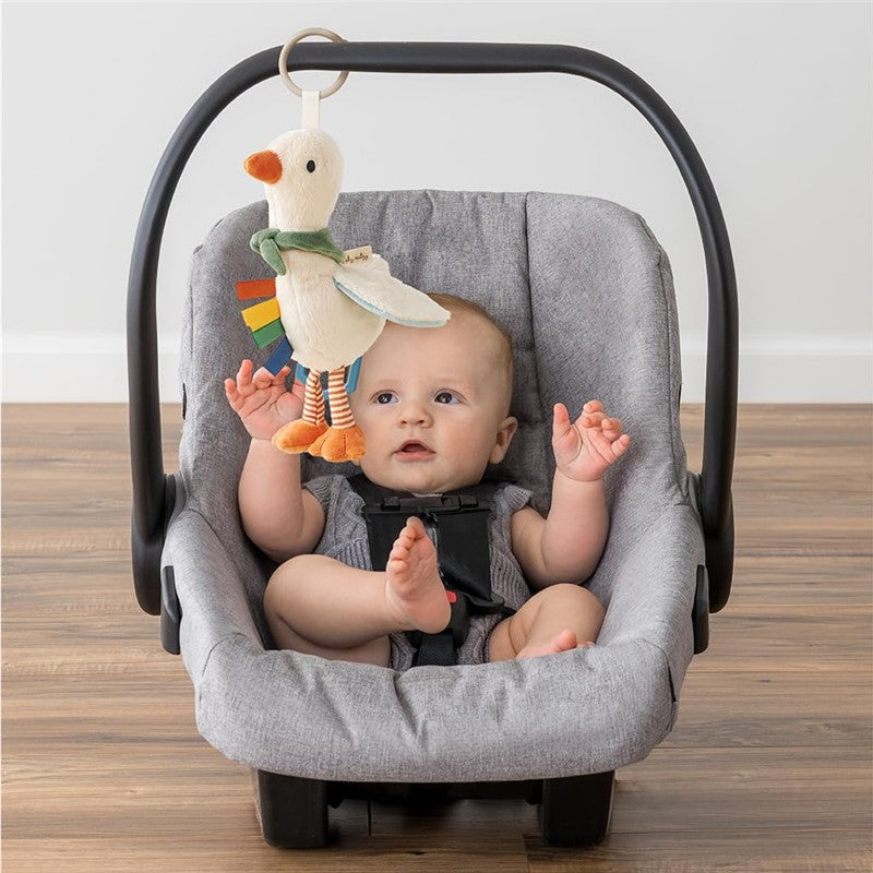 Baby in a car seat interacts with an Itzy Ritzy Bitzy Traveler toy, a soft, plush bird hanging above.