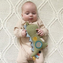Baby lying on a textured blanket, holding a green dinosaur plush toy with various colored tags and a mirror.