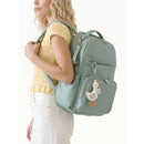 Mint green Itzy Ritzy Boss Plus™ Backpack Diaper Bag with a duck-shaped charm, worn by a woman in a yellow top and white pants.