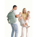 A family interacts joyfully outdoors with a man holding a green Itzy Ritzy Boss Plus™ Backpack Diaper Bag, featuring a cute duck keychain.