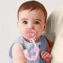 Baby with a pink bow silicone pacifier and clip, wearing a blue outfit, held by an adult.