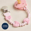Bow silicone pacifier clip in pink with a metal clip and flexible silicone beads, designed to keep pacifiers attached.