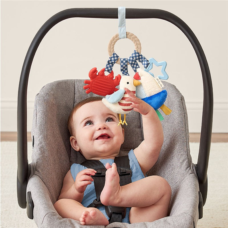 Baby in a car seat playing with the Itzy Ritzy Busy Ring teething toy featuring colorful sea creatures and birds.