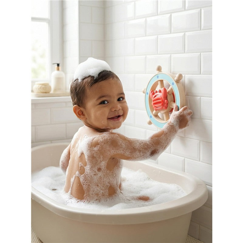 A smiling baby covered in bubbles plays with the Itzy Ritzy Captain Bath Steering Wheel, featuring a crab design, in a bathtub.