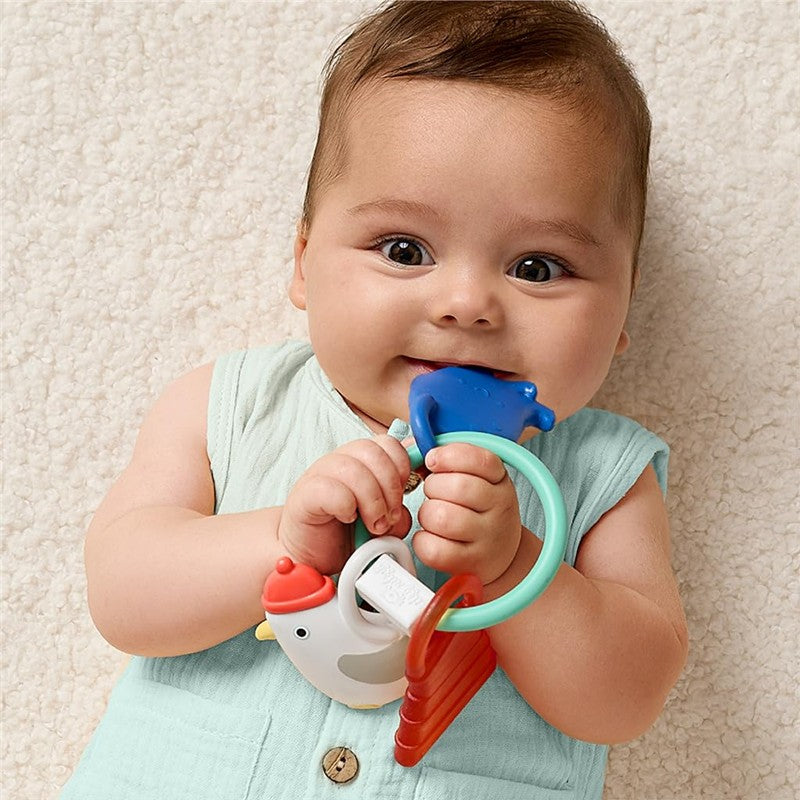 Baby holds the Itzy Ritzy Charms Multistage Teething Ring featuring colorful nautical-themed designs, smiling.