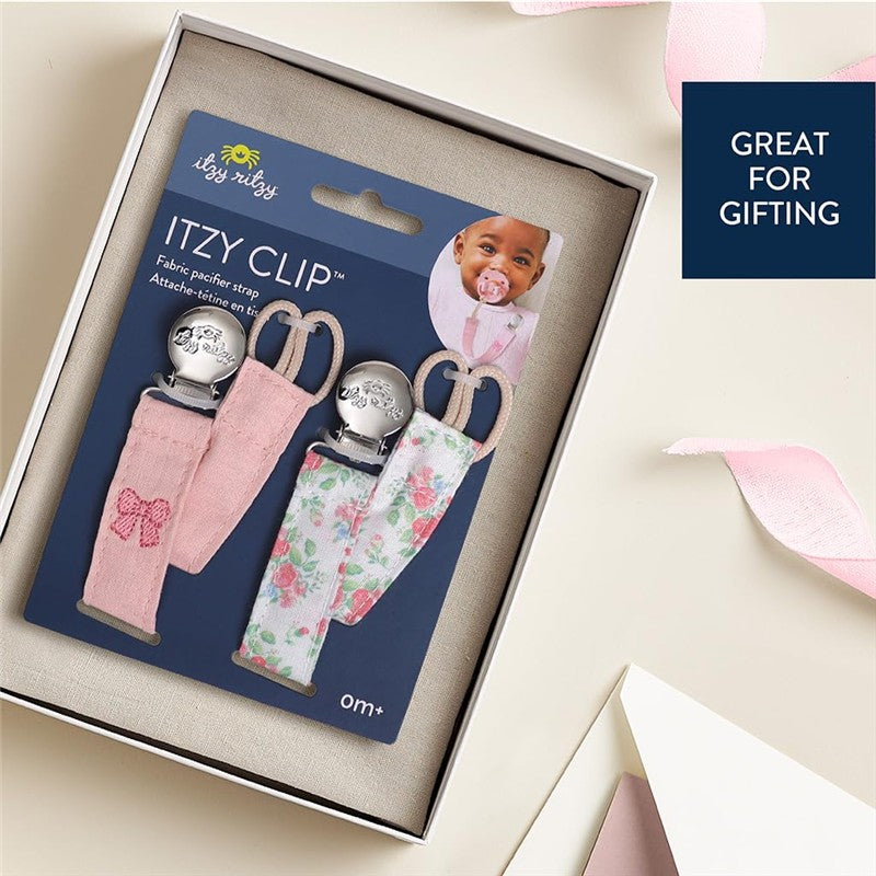 Itzy Ritzy Clip 2-Pack Fabric Pacifier Clips in pink and floral designs, displayed in a gift box with a baby image.