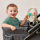 Toddler smiling while playing with the Itzy Ritzy Driver Travel Steering Wheel accessory attached to a stroller.