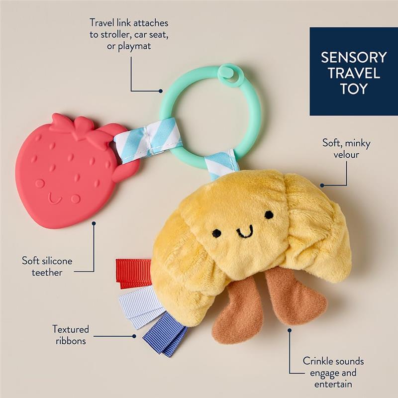 Infant teething toy featuring a soft croissant plush, a silicone strawberry teether, and textured ribbons for sensory engagement.