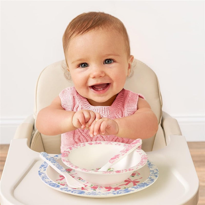 Smiling baby in a high chair, with a pink knitted top, surrounded by a floral Ribbons & Roses dining set.