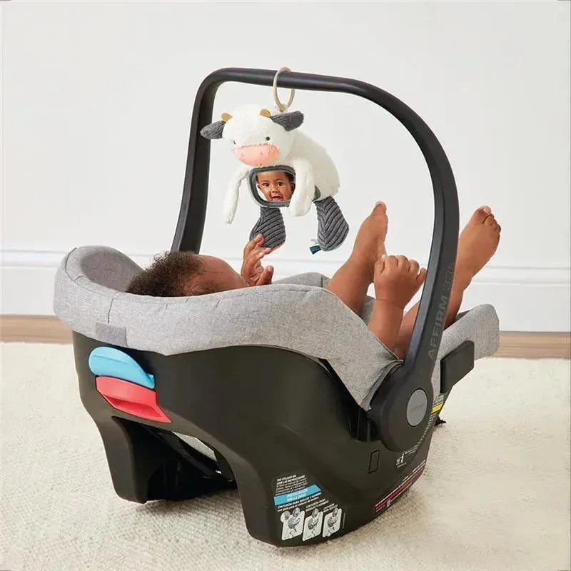 Itzy Ritzy Itzy Bitzy Mirror attached to a car seat, reflecting a smiling baby wearing a cow-themed hat.