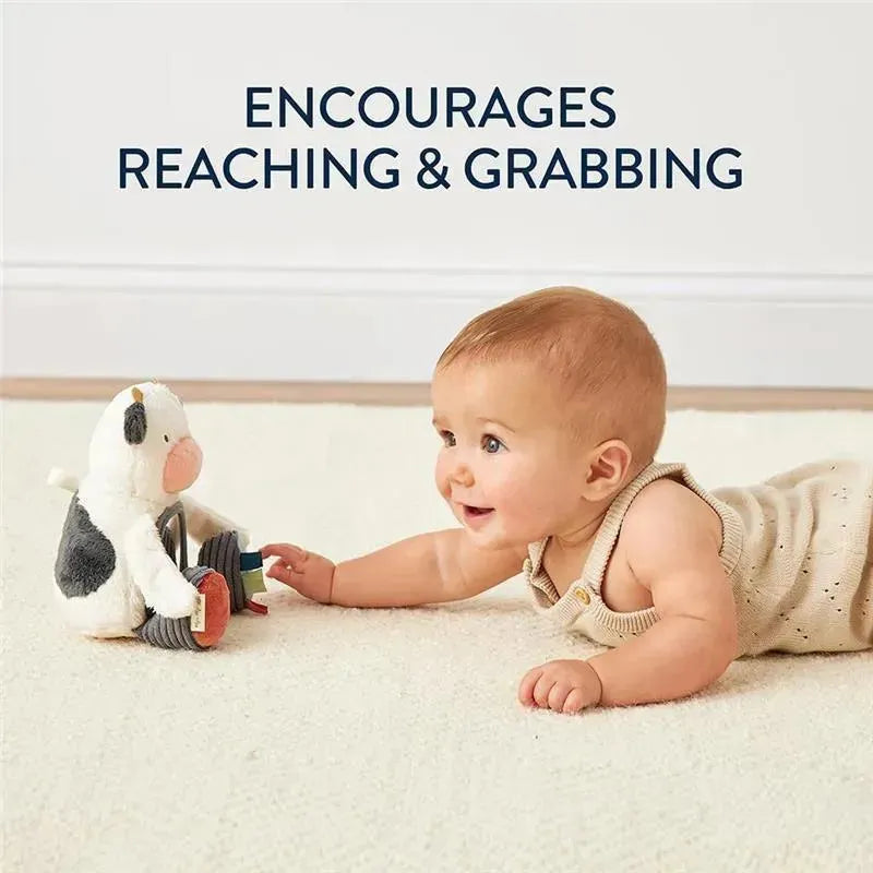 Baby reaching for a plush cow toy on a soft rug, promoting developmental skills with a focus on grabbing.