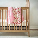 Itzy Ritzy Itzy Blanket™ in Strawberries + Cream draped over a wooden crib, featuring a pink border and strawberry print.