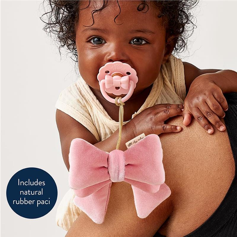 Baby holding a pink pacifier with a bow attachment, showcasing the Itzy Ritzy Itzy Blocks™ product.