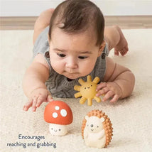 Baby reaching for colorful Itzy Ritzy Itzy Blocks™ toys, including a red mushroom and a hedgehog, on a soft surface.