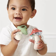 Toddler joyfully holding two Itzy Ritzy Mini Maracas designed as colorful mushrooms, smiling with delight.