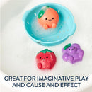 Three colorful bath toys in bubbly water: a smiling orange in a blue basket, a red strawberry, and a purple grape, promoting imaginative play.