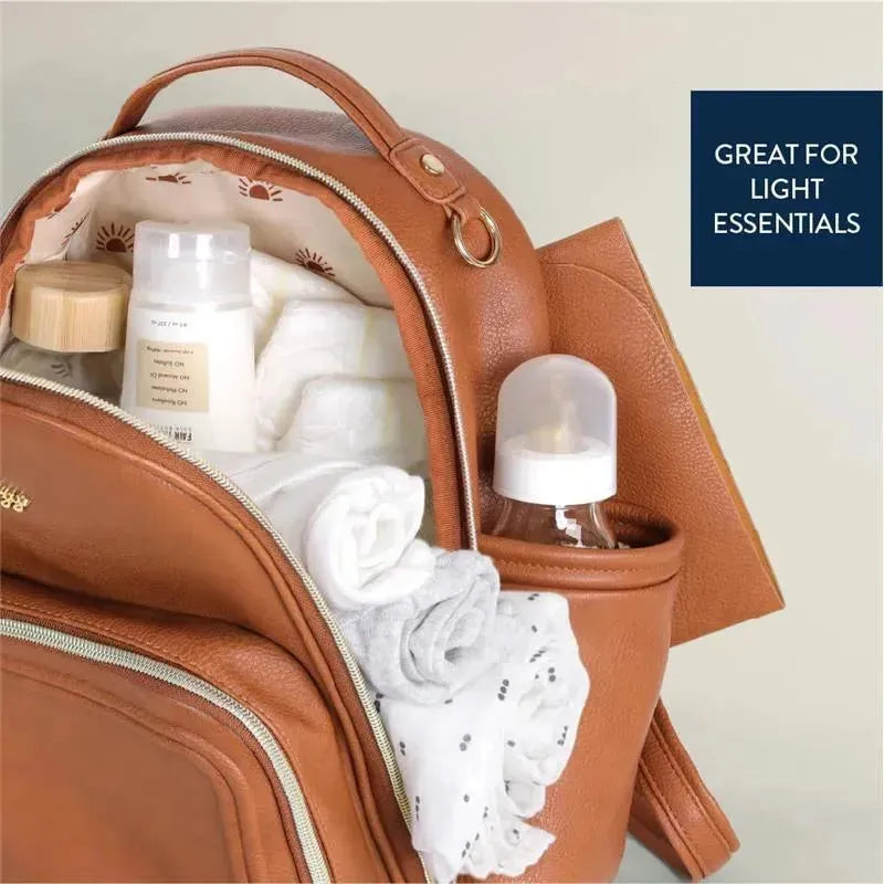 Cognac Itzy Ritzy Mini Plus Diaper Bag with essential items like baby bottles, wipes, and swaddles visible inside.