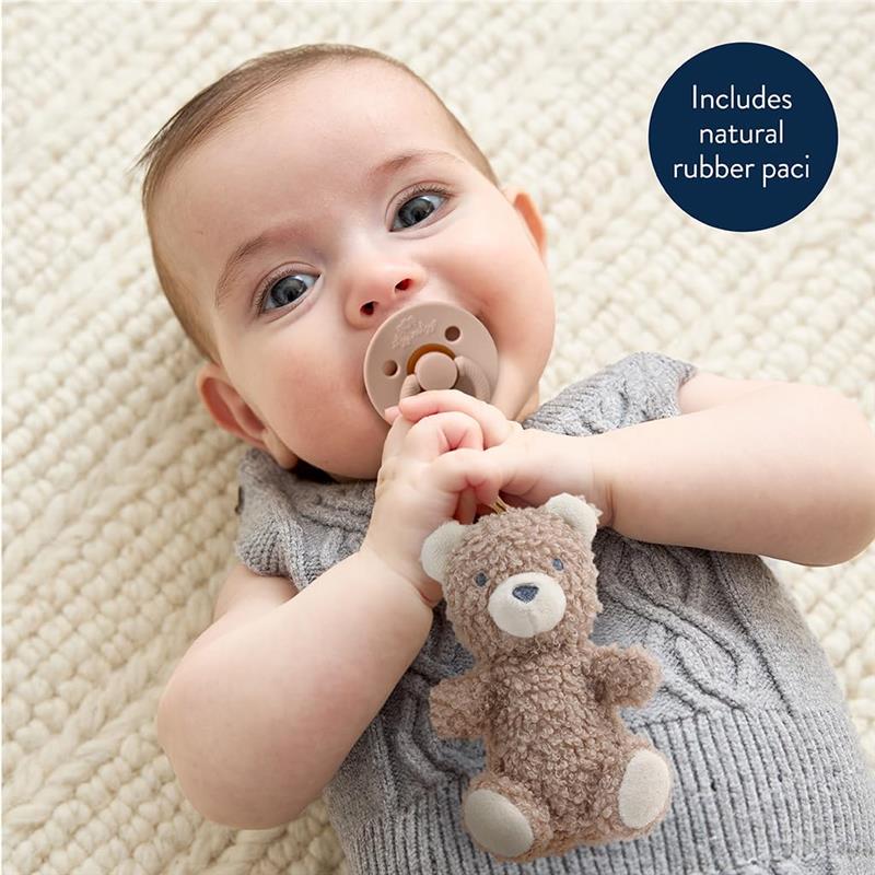 Baby lying on a textured blanket, holding a bear-shaped lovey and a natural rubber pacifier, with a soft smile.