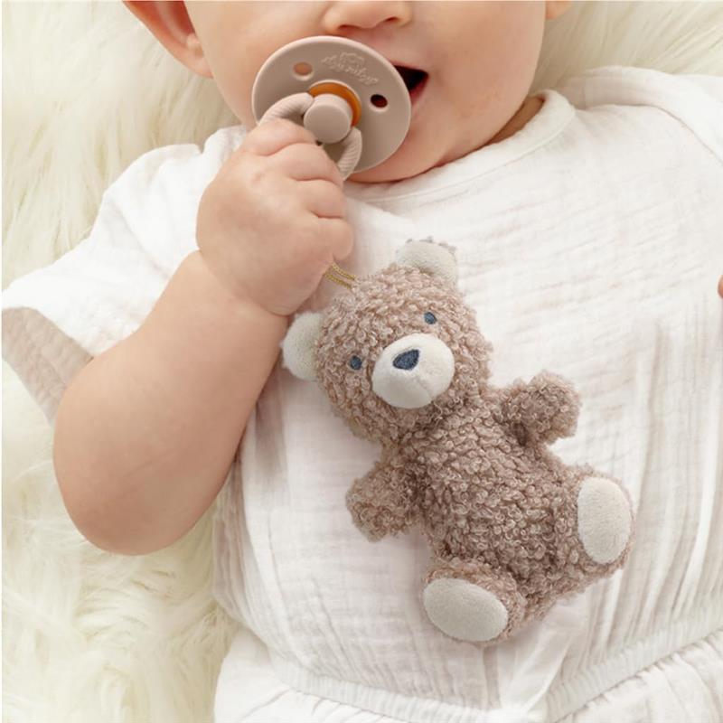 Baby holds an Itzy Ritzy bear pacifier and lovey set, featuring a soft, textured bear and a soothing pacifier.