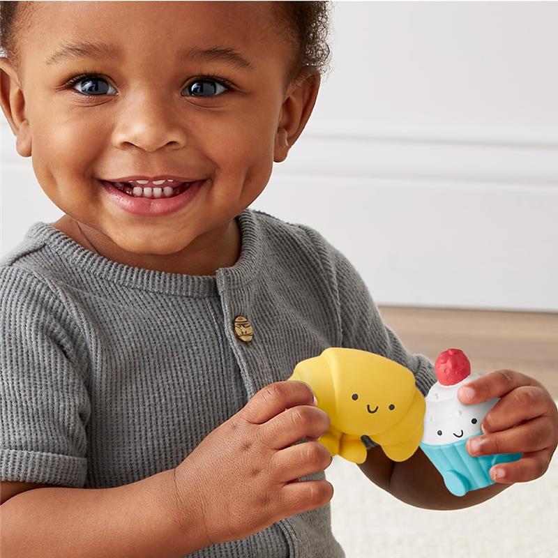 Toddler smiling while holding a yellow croissant and a blue ice cream toy from the Itzy Ritzy bakery activity set.