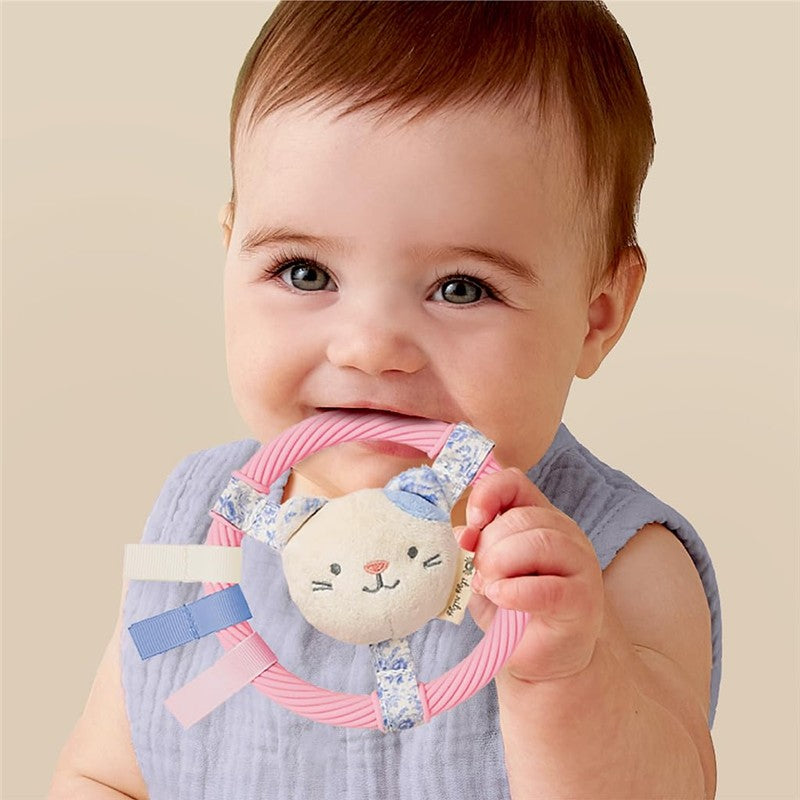 Baby smiling while holding a pink Itzy Ritzy Ring Pal teething ring featuring a plush kitty face and colorful fabric tags.